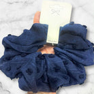 Navy pompom-textured scrunchie in hand, perfect for stylish hair ties or a cozy wrist accessory.