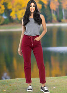 Woman wearing Judy Blue Bridget Joggers in crimson with a drawstring waistband, standing in a park with autumn trees and a lake.