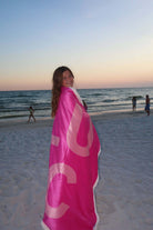 Woman smiling on the beach wrapped in the LM-BK LULU MAC BLANKET PINK during sunset.