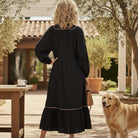 Back view of a woman in a GRACEFUL INSTINCTS MAXI DRESS with balloon sleeves, standing next to a golden retriever.