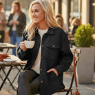 Model wearing WARM IMPRESSIONS BUTTON DOWN shacket while enjoying coffee at a cafe, showcasing cozy style.