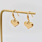 Forever Yours Earrings - 18K gold-plated heart drop earrings on a display stand, perfect for everyday wear.