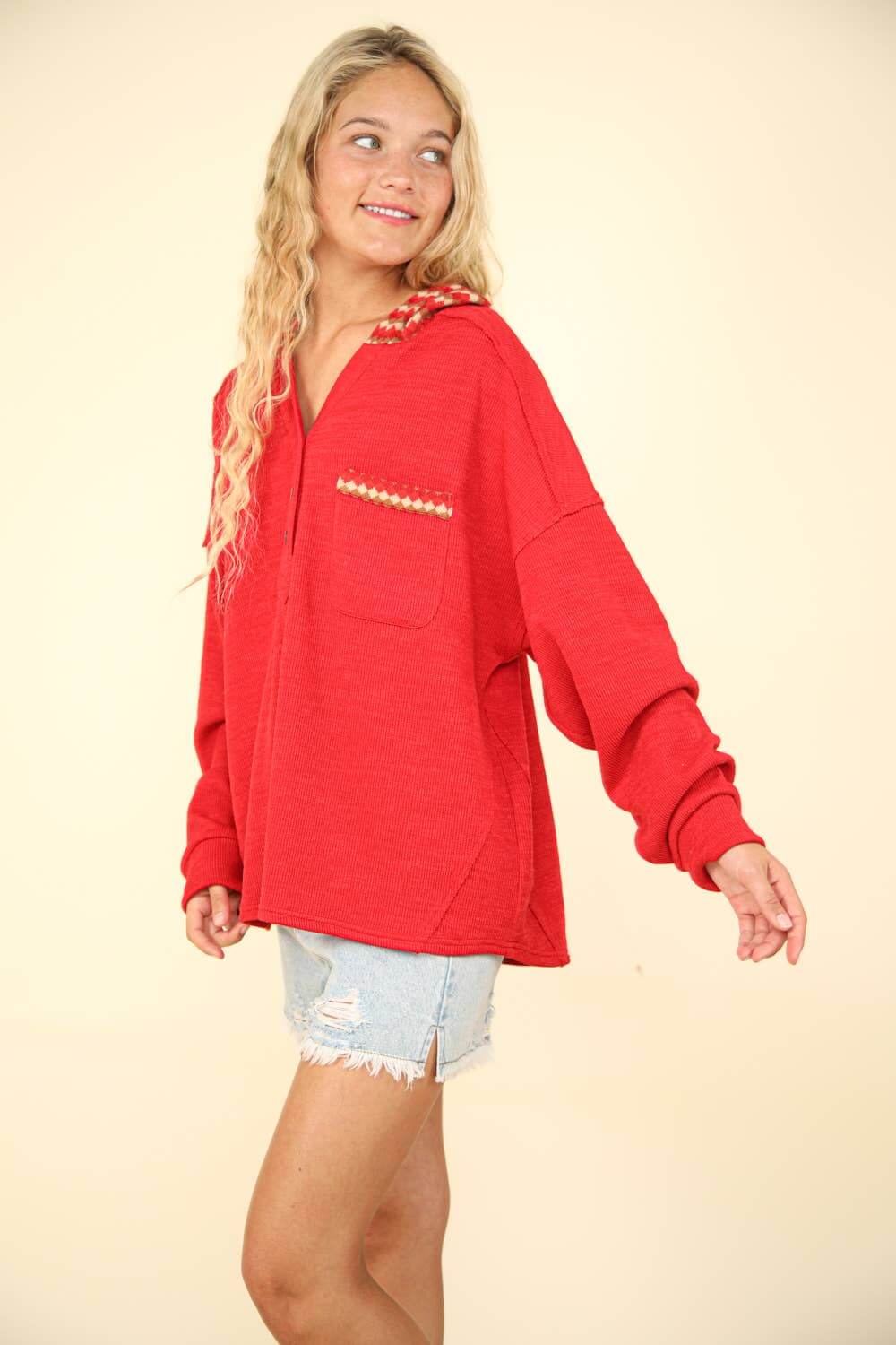 Model wearing oversized red contrast hoodie with pocket, styled with denim shorts, showcasing a cozy knit top.