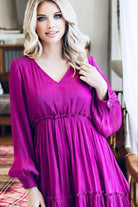 Woman wearing magenta Bermuda Beauty Dress with v-neckline and balloon sleeves in elegant setting.