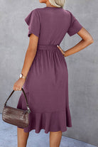 Back view of a woman in a purple midi dress with petal sleeves and a belted waist, styled for casual outings.