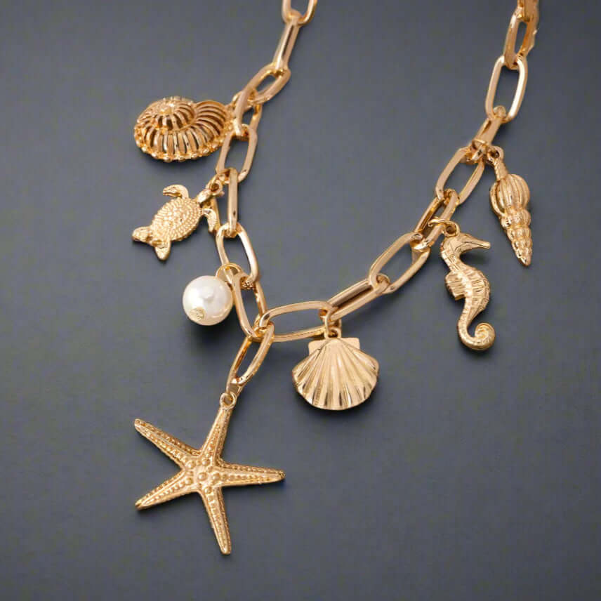 Gold tone charm necklace featuring starfish, turtle, scallop shell, pearl bead, and seahorse charms.