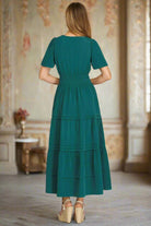 Woman wearing teal green She+Sky FLEETING MOMENT Dress with tiered pintucks, elastic waist, and side pockets in elegant setting.