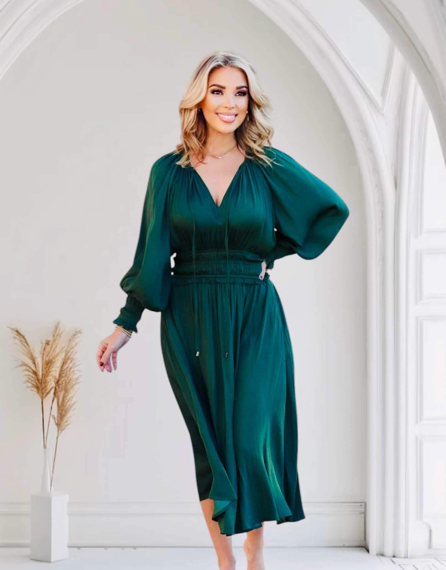 Woman wearing dark green midi dress with smocked sleeves and waist, posed in a stylish white interior.