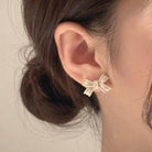 Elegant bow-shaped earrings with faux pearls, showcased on a model's ear for a classic look.