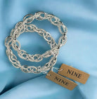 Silver stretch chain link bracelet by Nine Jewelry on a blue background, featuring smooth and textured interlocking designs.