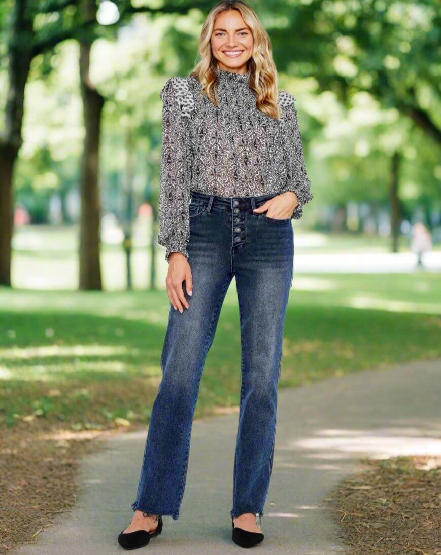 Model wearing Judy Blue Ava Jeans in a park, showcasing high-rise, distressed denim with a stylish top.
