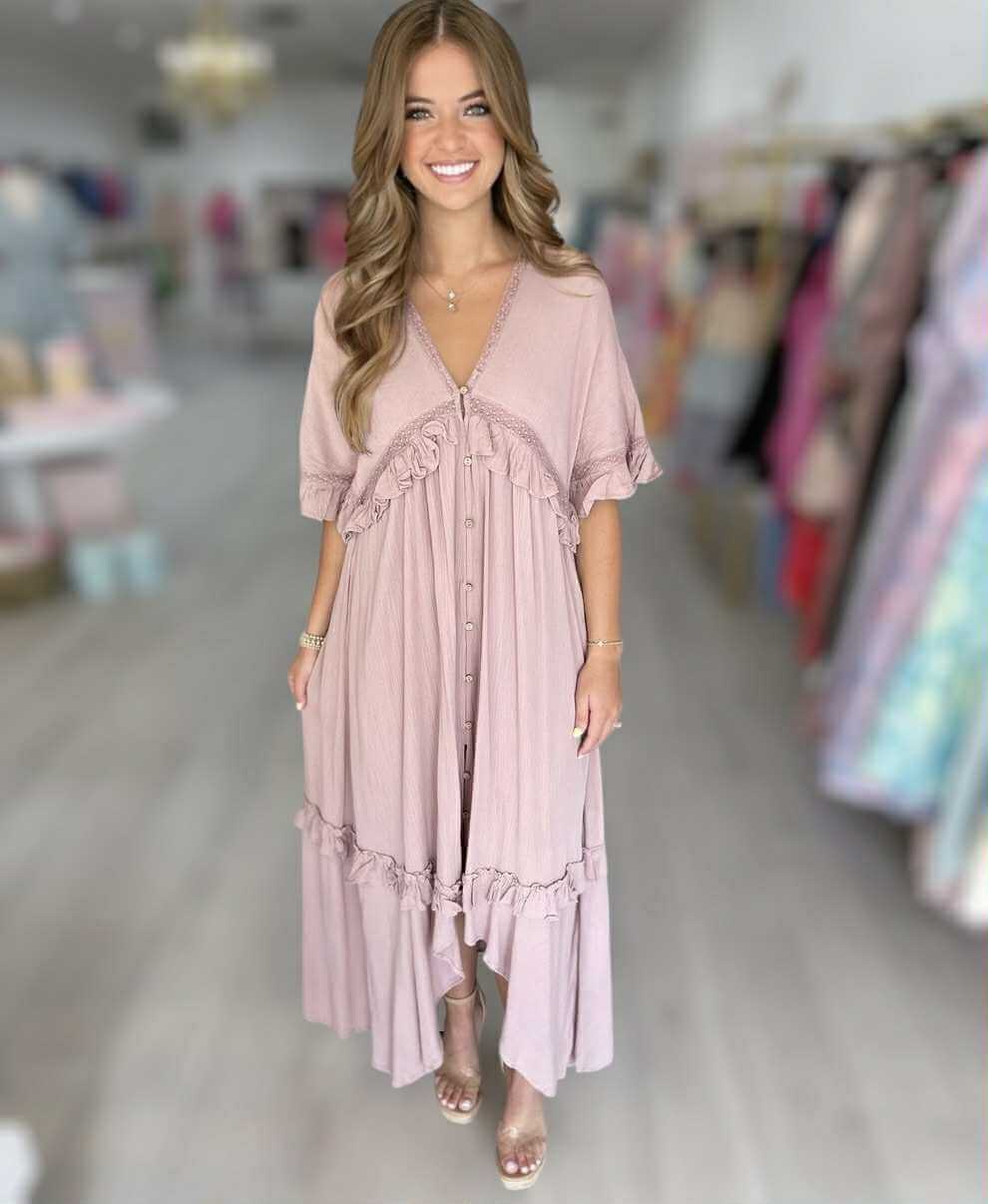 Model wearing blush Ever After Maxi Dress with ruffles and lace in a boutique setting.