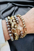 Taupe gray Serene Bracelet Set by Nine Jewelry featuring gold-toned quatrefoil and faceted bead bracelets on a wrist.