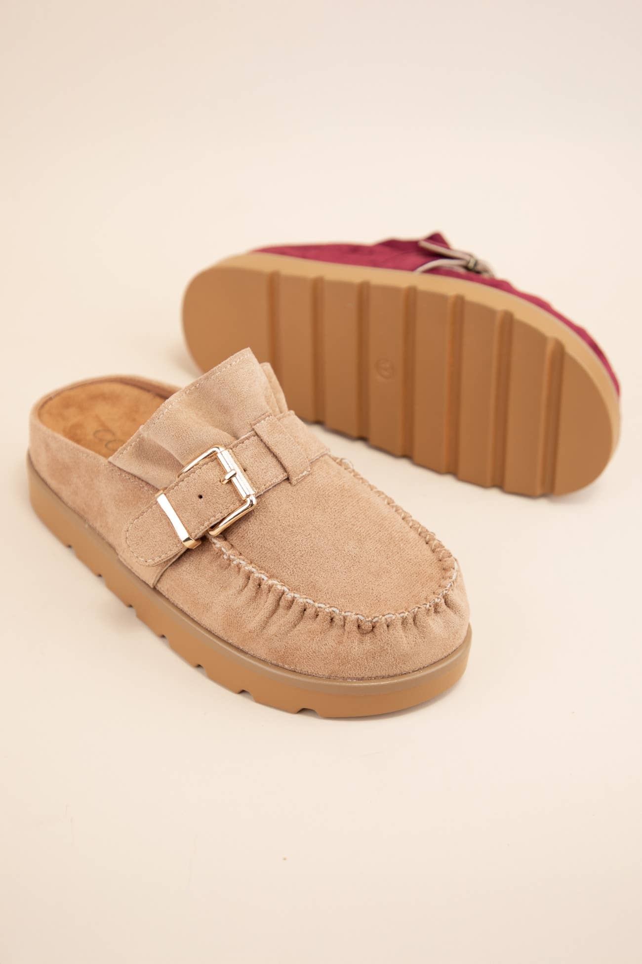 Comfortable beige slip-on moccasin mule with buckled strap and stylish ruffle design, perfect for chic and effortless wear.
