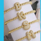 Gold-tone rhinestone initial bracelets featuring bold bubble letters on a wrist, sparkling for personalized glam.