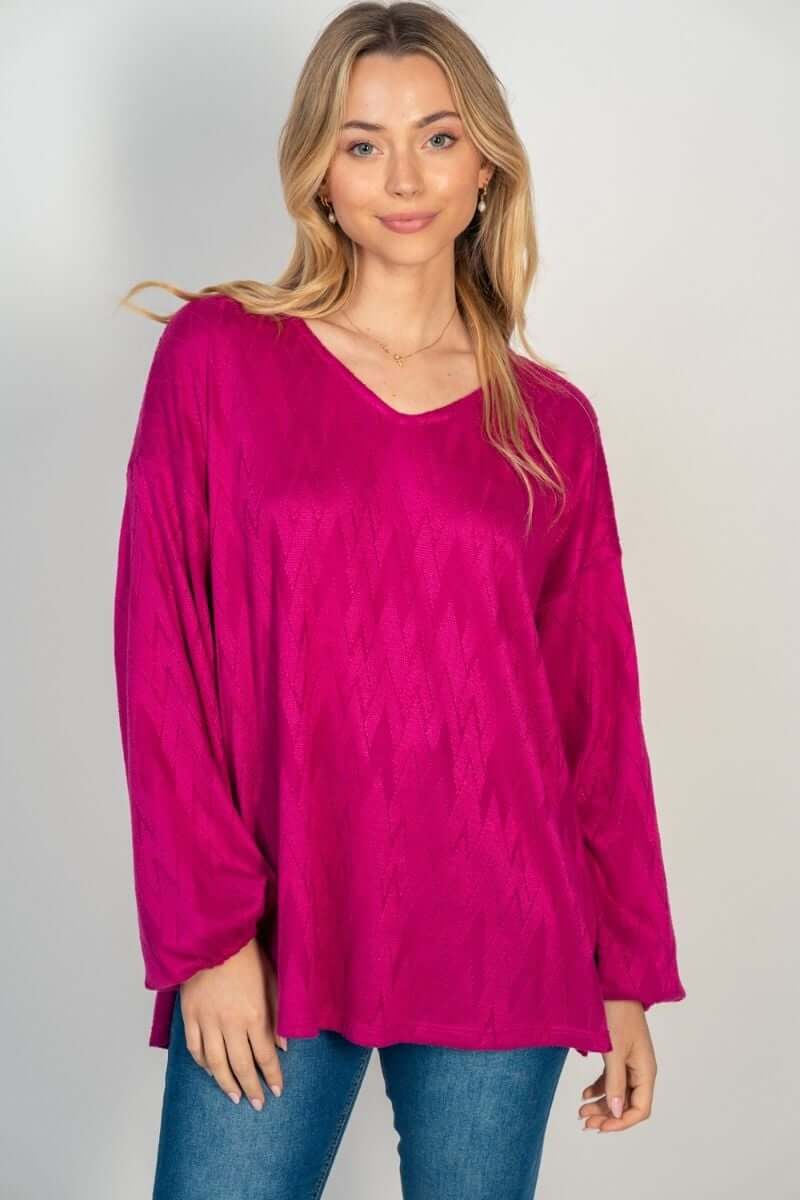 Woman wearing HAPPY WANDERER hot pink long sleeve top with woven pattern by White Birch, showcasing V-neck and side split design.