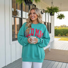 LULU MAC Aqua with Coral Puff Logo Crew sweatshirt model holding a drink in a cozy outdoor setting.