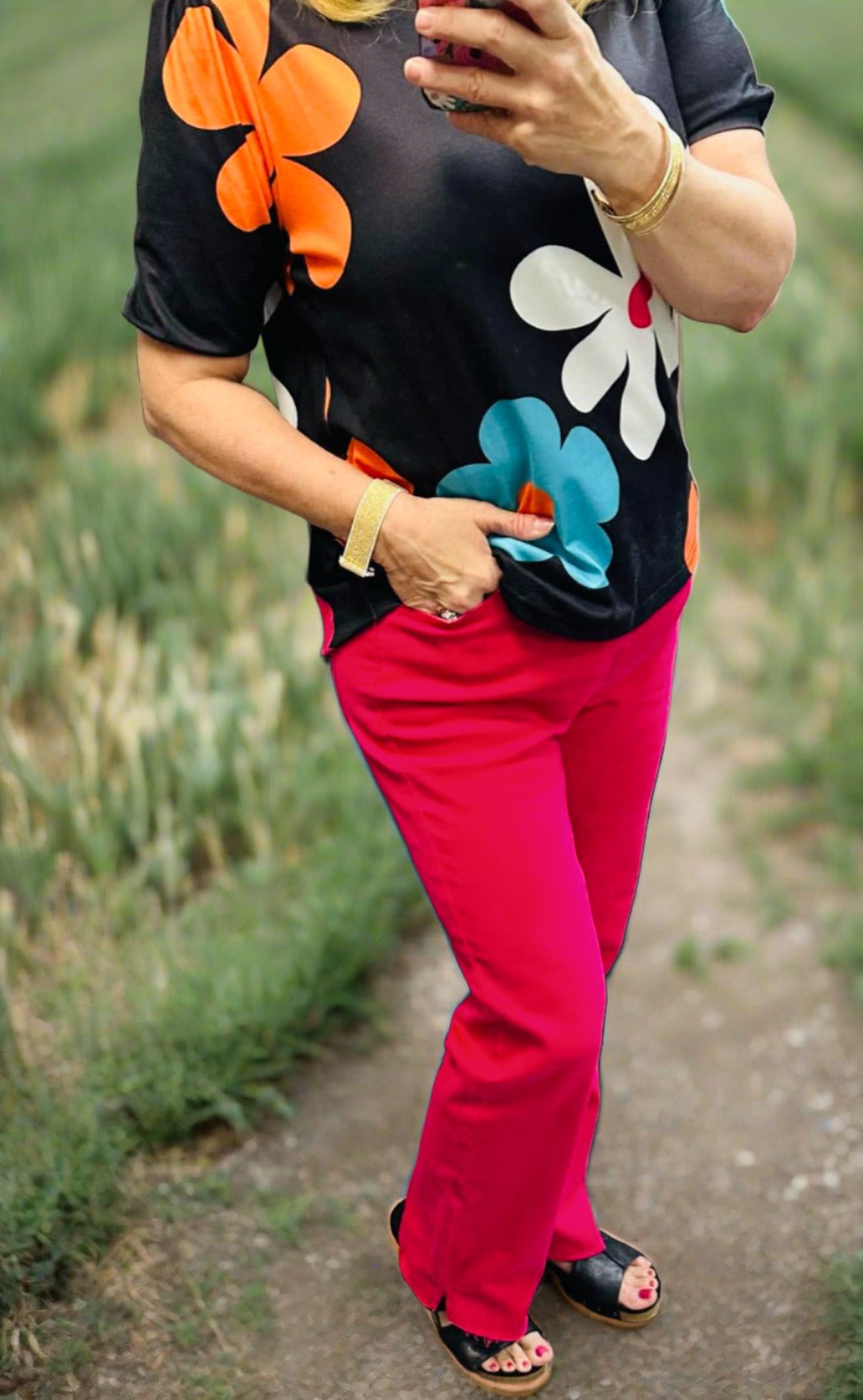 Woman wearing colorful floral top and fuchsia tummy control jeans walking on a country path.