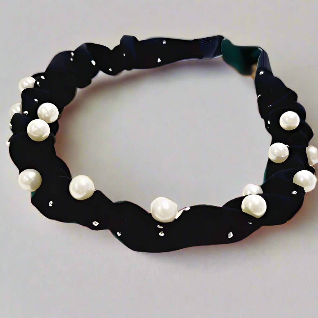 Wrinkled Pearl Accent Headband featuring pearls on a black fabric, displayed on a textured round mat. Assorted pack of 12 units.