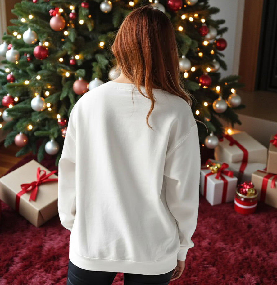 Woman wearing the WOODLAND WONDERLAND PULLOVER in white, standing in front of a Christmas tree with holiday decorations.