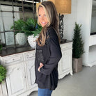 Model wearing CITY LIGHTS TOP, a black corded shacket with sequin patch pocket, styled casually in a bright interior.
