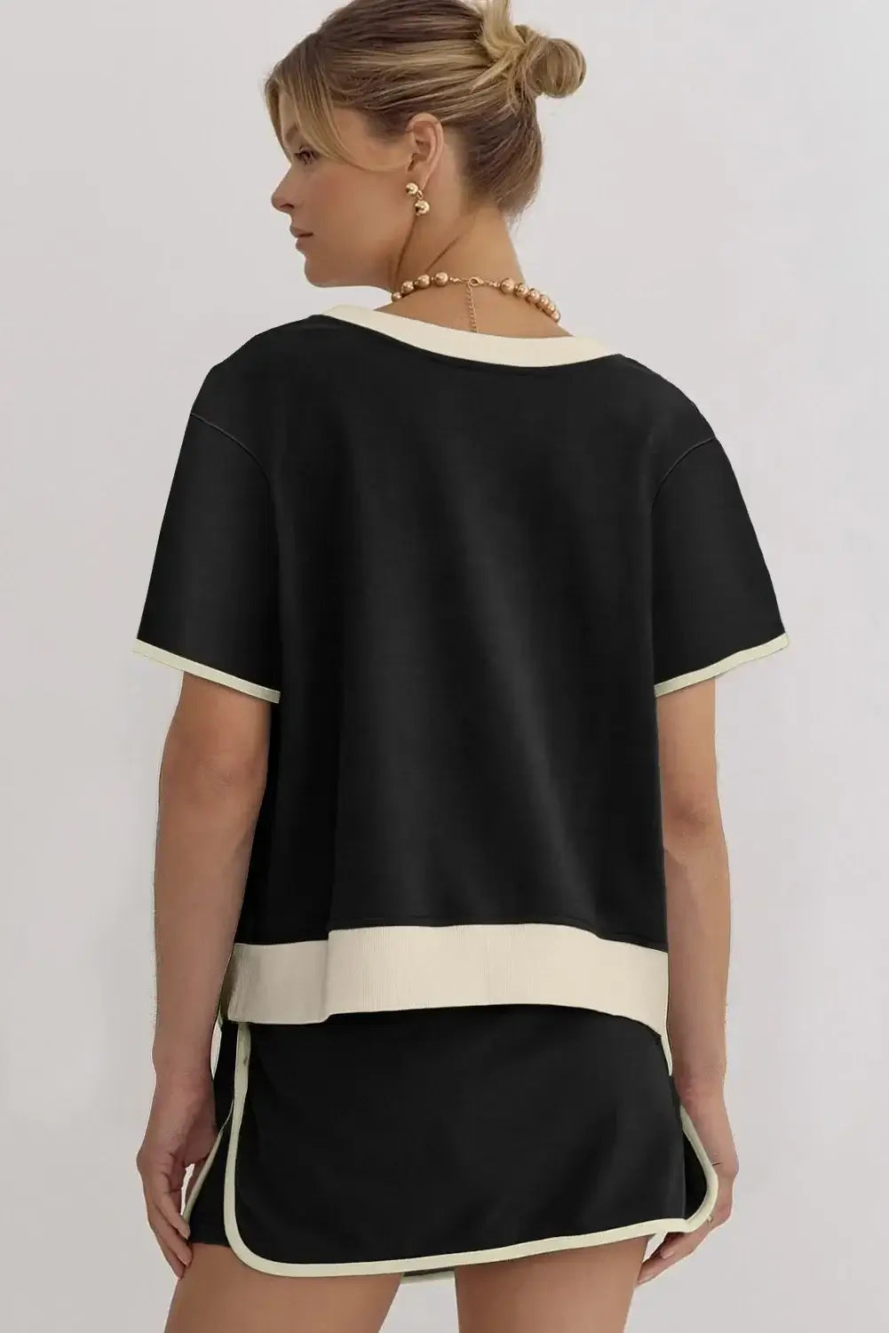 Back view of a woman in the black Boardwalk Breeze Skort Set, featuring a relaxed-fit top and drawstring skort.