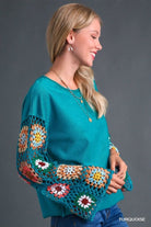 Woman wearing turquoise Flower Child Crochet Sleeve Top with colorful crochet details and raw hem, side view.