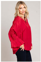 Woman wearing red VIP ACCESS top from Cotton Blue with bell sleeves and eyelet details, perfect for holiday wear, made from rayon blend.