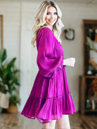 Woman wearing magenta Bermuda Beauty Dress with balloon sleeves and v-neckline in a stylish indoor setting.