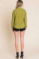 Back view of a woman in an olive green embossed shacket paired with black shorts and ankle boots.