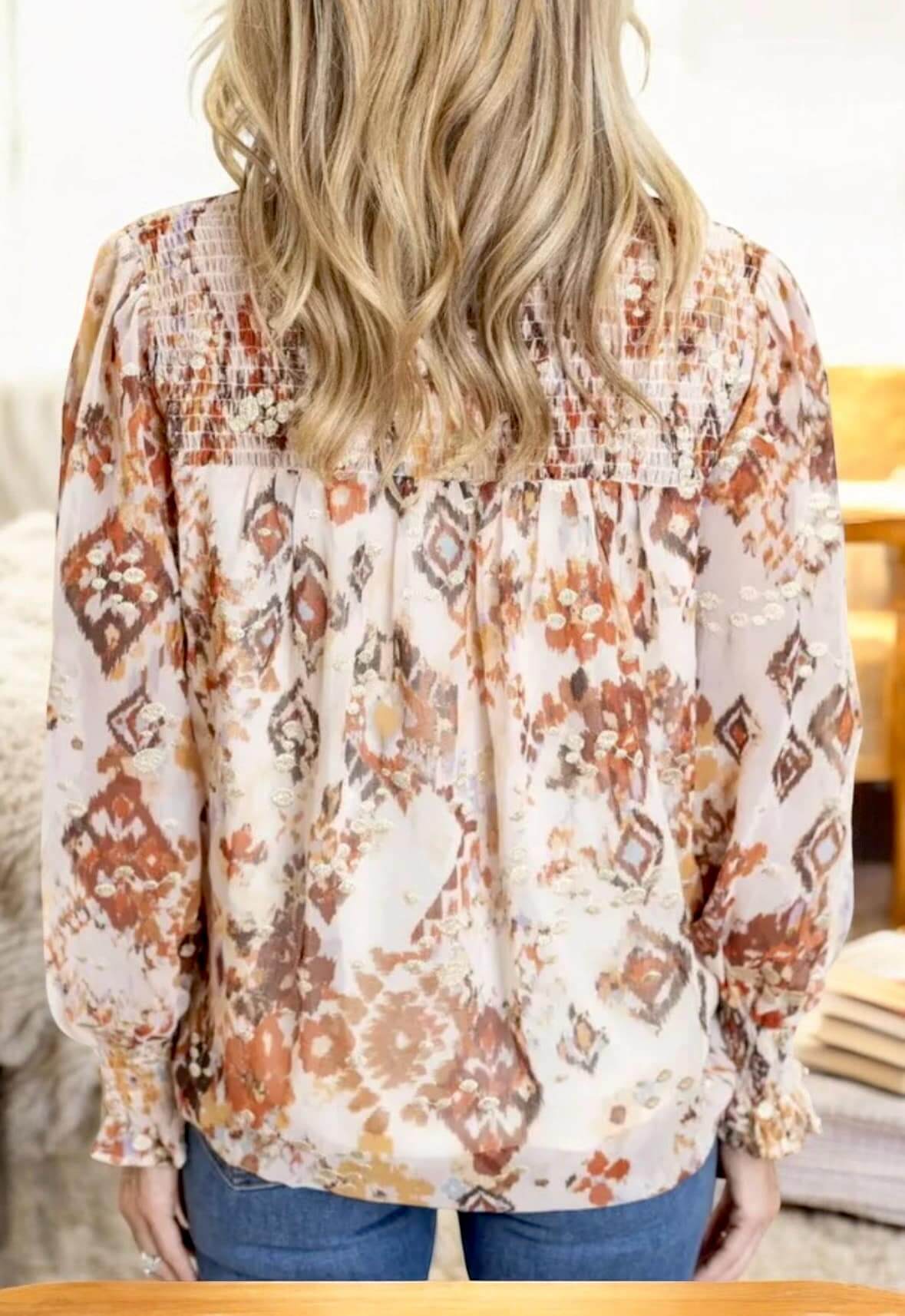 Back view of a woman wearing a beige and brown patterned top with smocked sleeves and elegant details.