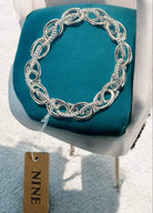 Silver UPLINK BRACELET by Nine Jewelry on chair, featuring interlocking chain links with smooth and textured designs.