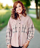 Woman wearing light pink velvety top with plaid sleeves and pockets, stylishly posed outdoors, showcasing fashion-forward design.