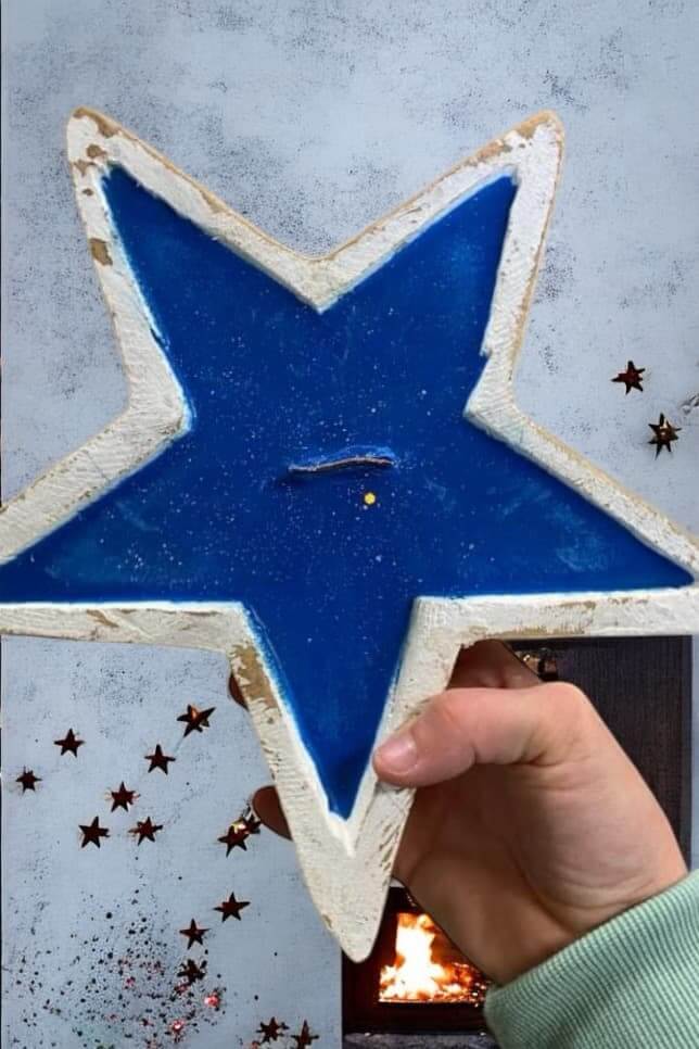 Hand holding a blue star-shaped candle in rustic dough bowl with mahogany teakwood scent, farmhouse decor on starry background.