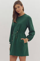 Woman wearing the dark green EVERGREEN BREEZE dress with drawstring waist, long sleeves, and pockets, showcasing a stylish, comfortable look.