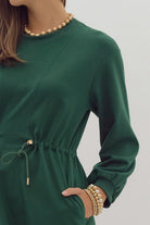 Evergreen Breeze dress by Entro in dark green with a drawstring waist and side pockets, worn with gold accessories.