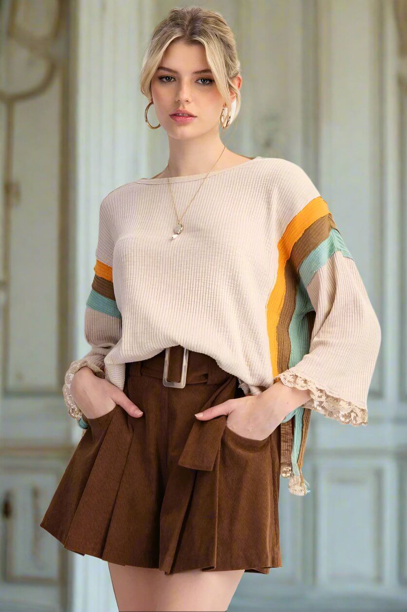 Woman modeling the KEEP THE FAITH top with striped sleeves, lace hem, and side slits, paired with a brown skirt.