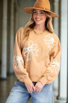 Woman wearing BOWS AND DREAMS top, beige terry knit pullover with bow detailing, paired with jeans and a hat, in a relaxed fit.