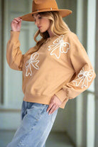 Woman wearing a cozy tan pullover with bow detailing and a hat, showcasing a relaxed fit and stylish look.