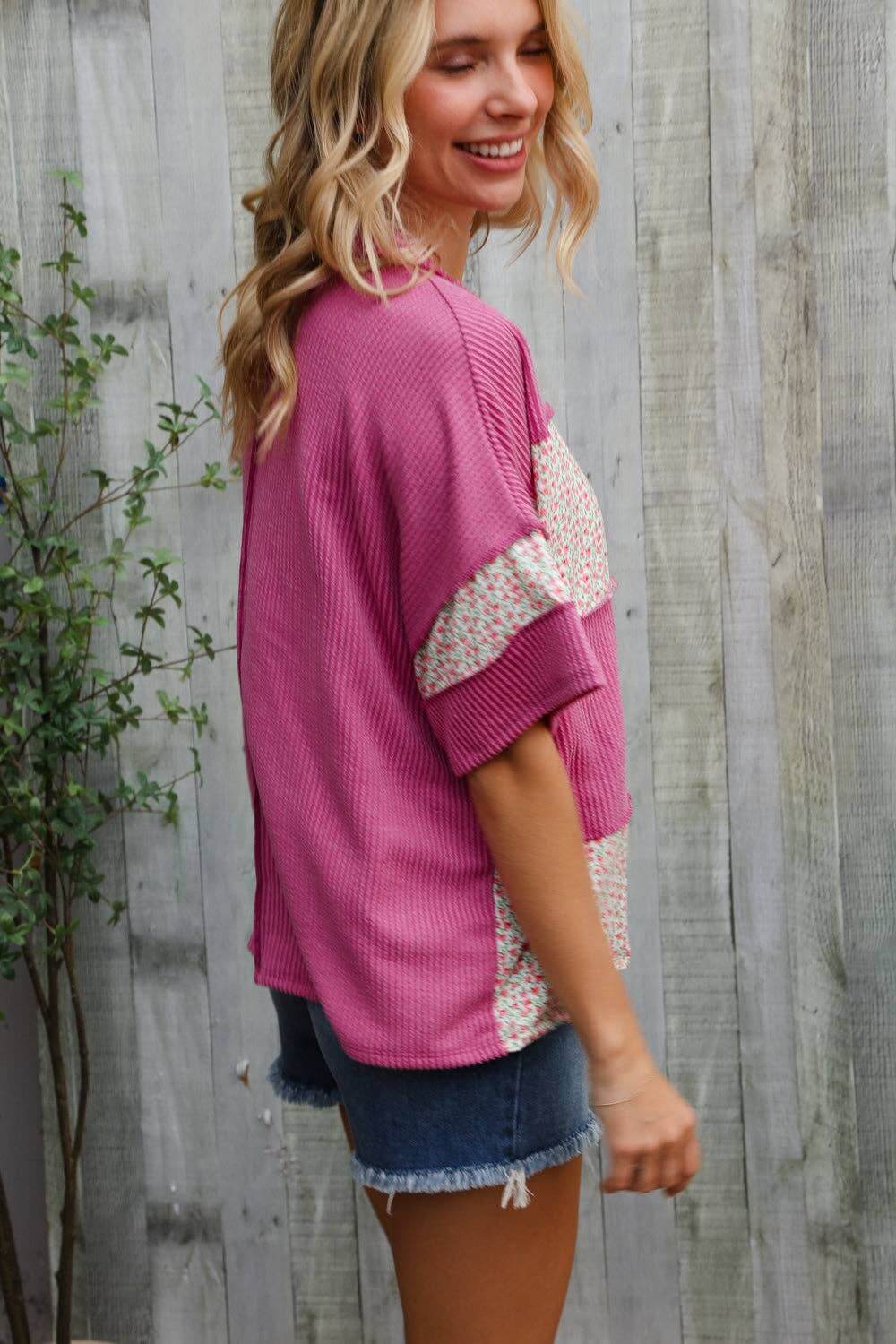 Woman in fuchsia floral wavy rib pullover and denim shorts, showcasing trendy color block style.