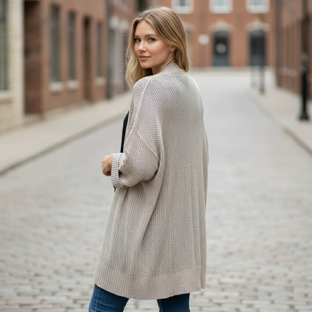 Woman wearing BAREFOOT MORNINGS CARDIGAN, standing casually in a cobblestone street, showcasing its relaxed style.