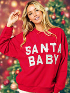 Woman wearing red SANTA BABY crewneck sweatshirt with festive Christmas tree background