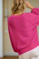 Woman wearing pink STAY POSITIVE sweater by Umgee with exposed seams and ribbed waistband, showcasing back view.