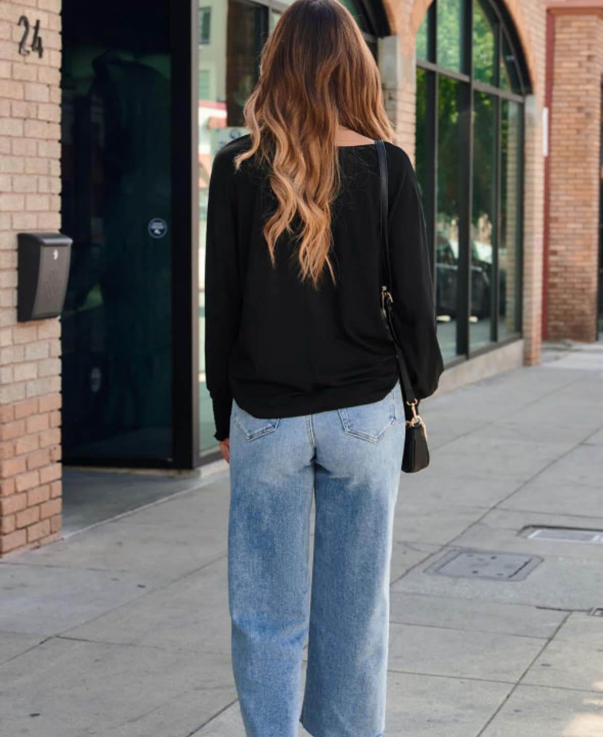 Woman wearing the JET SET TOP in black with wide-leg jeans, showcasing a casual street style look.