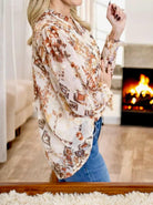 Beige and brown smocked sleeve top with gold dots, displayed by a model beside a glowing fireplace.