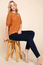 Model wearing a copper puff sleeve Field of Daisies Top, paired with dark jeans and sitting on a wooden stool.
