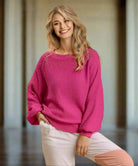 Woman wearing pink STAY POSITIVE sweater by Umgee with long sleeves and round neck, styled with white pants in elegant setting.