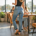 Model wearing JUDY BLUE - AVERY JEANS in a cafe, showcasing the relaxed boyfriend fit and modern release hem.