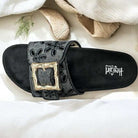 Black slide sandals with eyelet embroidery and oversized bamboo-style buckle by Corkys.