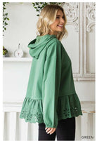 Woman wearing green ADVENTURE AWAITS Hoodie Top with eyelet ruffle and long sleeves, stylish and cozy oversized design by Cotton Bleu.